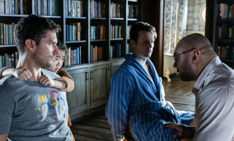 Two men are tied up with their frightened child behind them as another man talks to them.