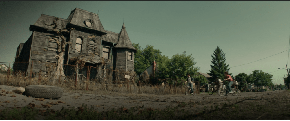 four children on bikes look up at an old house that is falling down