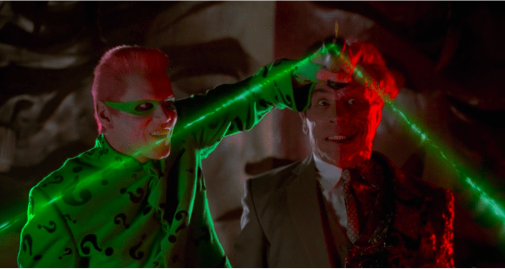 a man in a green suit grasps the head of another man in a business suit