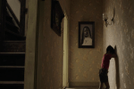 a boy leans against a wall covering his eyes in a hallway with a large portrait hanging overhead