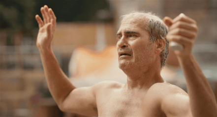 A shirtless man who looks upset raises his hands in surrender